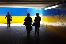 people walking through tunnel painted like Ukrainian flag