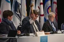 man swinging gavel in front of flags