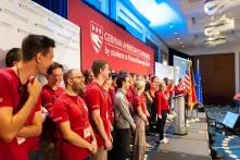 group of students in red shirts standing on a stage in front of a banner that says "german american conference"
