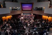 crowd in hall with large screen above them