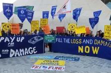 protest at COP28, protestors holding many signs and banners demanding loss and damage funding
