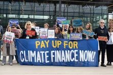 protestors hold up a banner that says "pay up for climate finance now!"