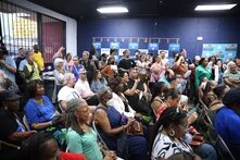 people stand or sit in a campaign office with a blue wall in the background