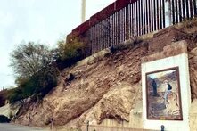 A metal fence on top of a cliff with a mural of a child riding a donkey on the cliff