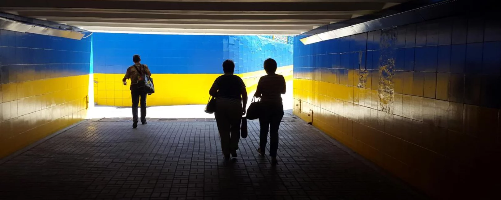 people walking through tunnel painted like Ukrainian flag