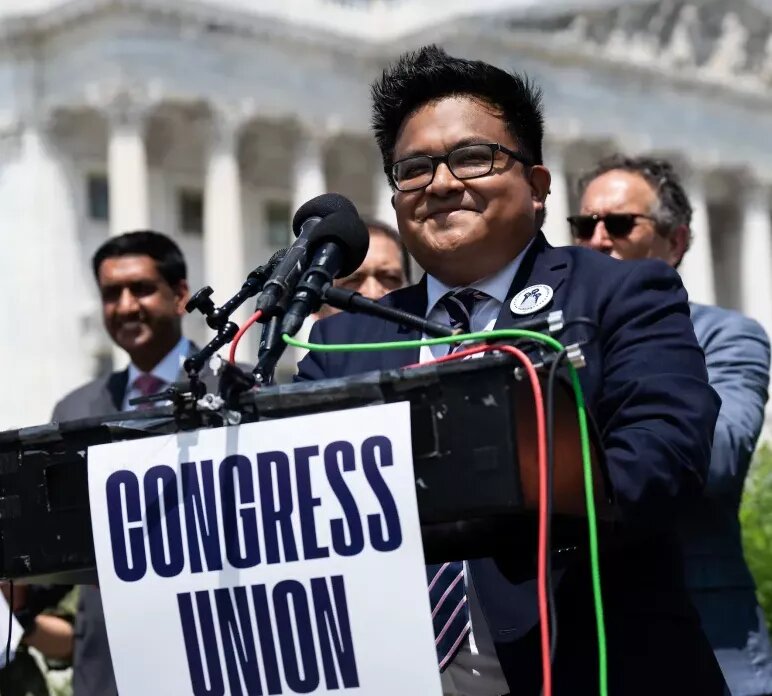 man standing at a podium with microphones and a sign that says "congress union" in front of the Capitol Building