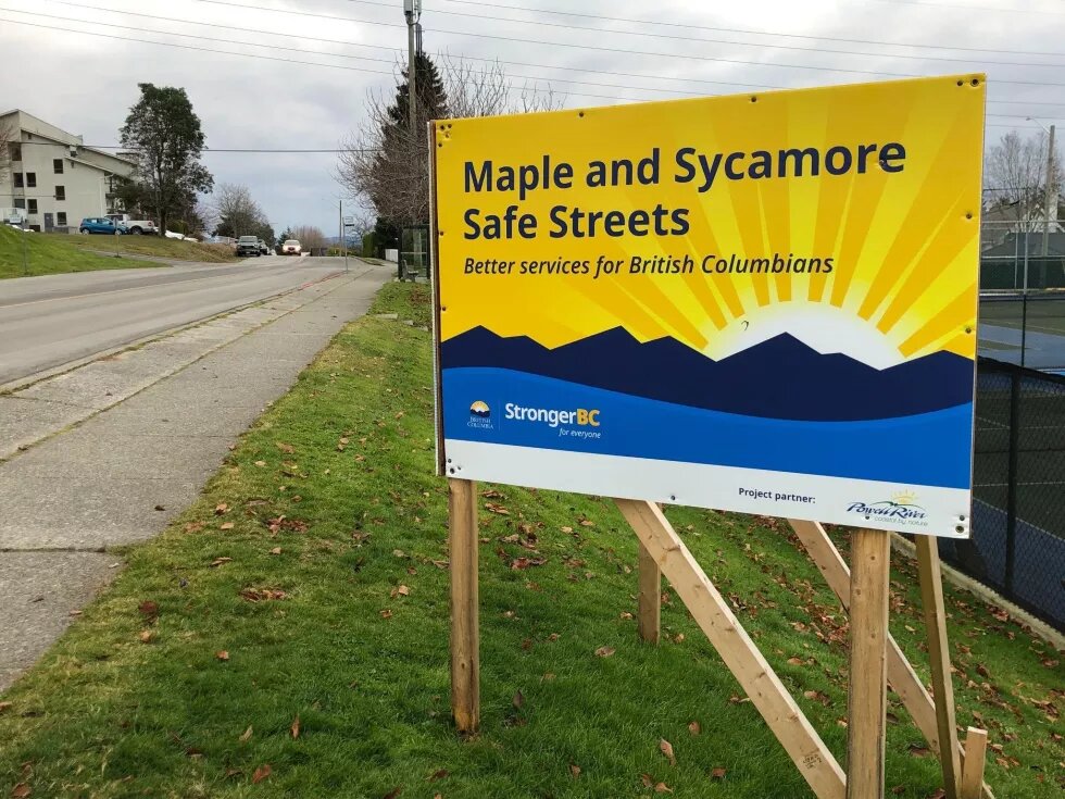 Sign next to road that says "Maple and Sycamore Safe Streets: Better services for British Columbians"