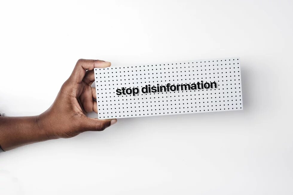 a hand holds a sign that says "stop disinformation" over a white background