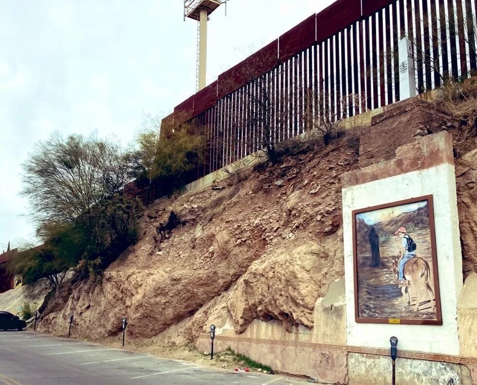 A metal fence on top of a cliff with a mural of a child riding a donkey on the cliff