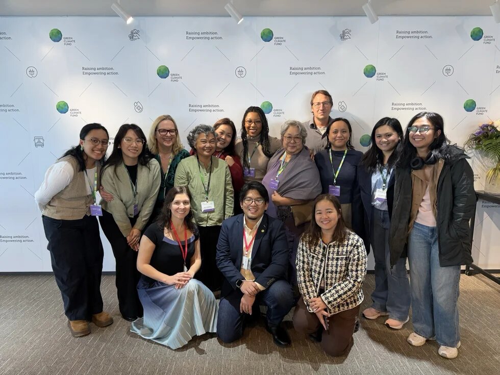 a group of people stand in three rows in front of a wall with the Green Climate Fund logo